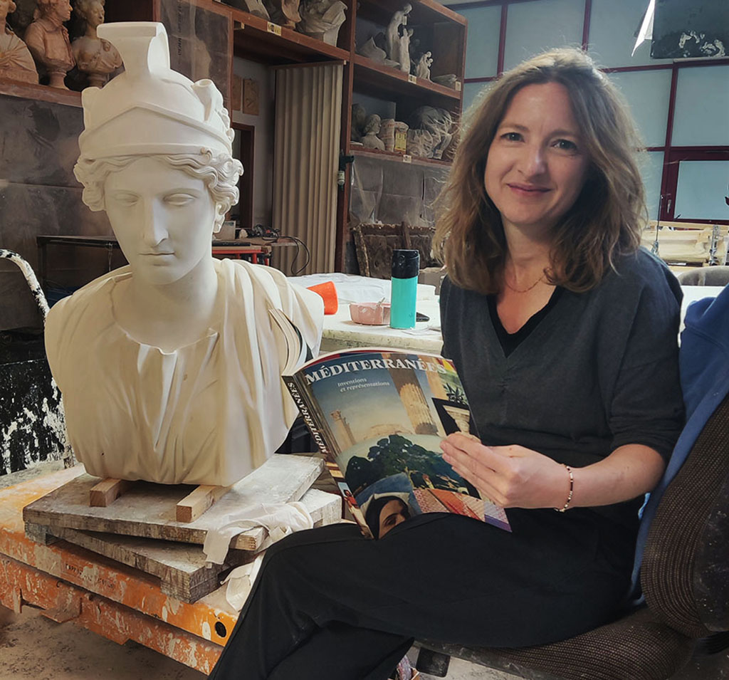 Laure Lane photographie au sein des ateliers d’art GrandPalaisRmn. Elle tient le catalogue ouvert dans ses mains